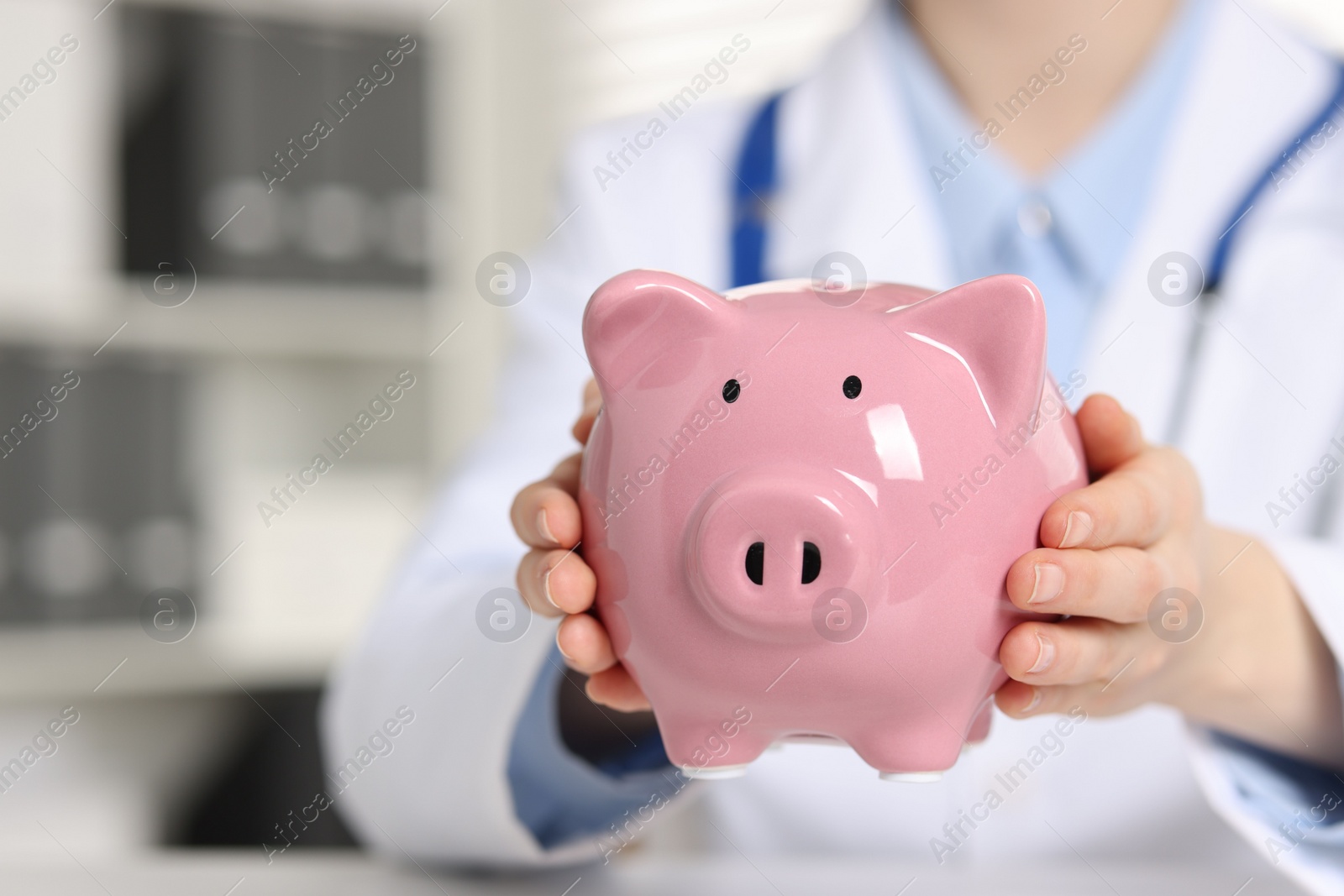 Photo of Doctor with piggy bank at white table indoors, closeup. Space for text