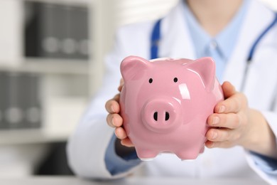 Photo of Doctor with piggy bank at white table indoors, closeup. Space for text