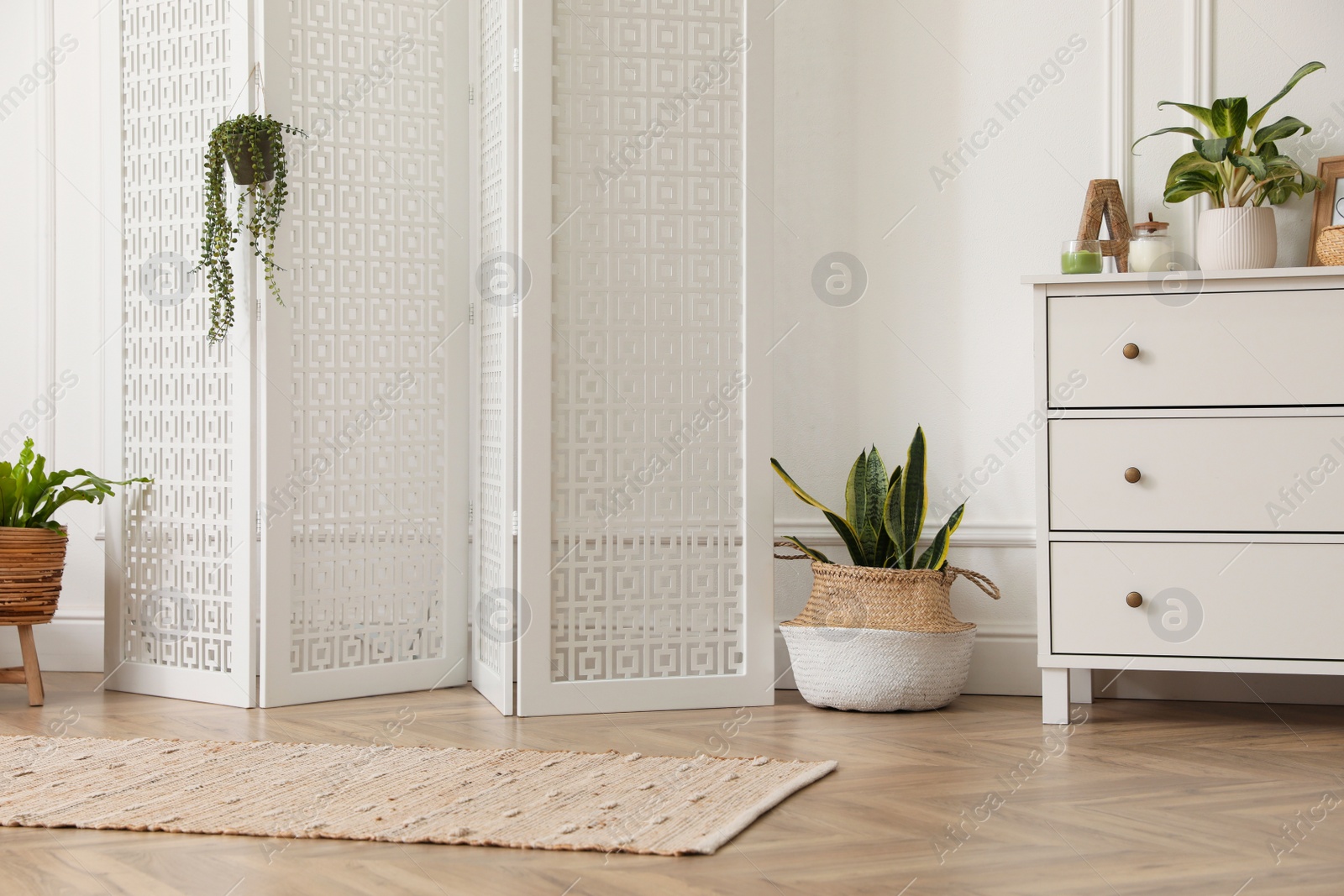 Photo of Stylish room with wooden folding screen and chest of drawers near white wall. Interior design