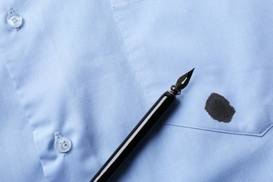 Black ink stain on light blue shirt and pen, top view. Space for text