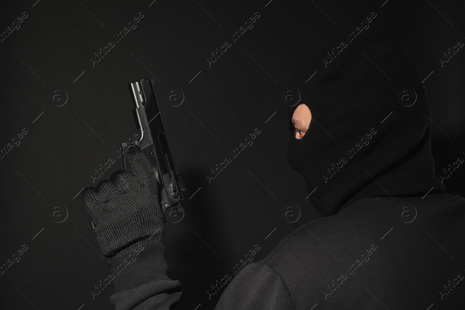 Photo of Dangerous masked criminal with gun on black background. Armed robbery