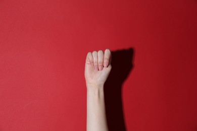 Photo of SOS gesture. Woman showing signal for help on red background, closeup