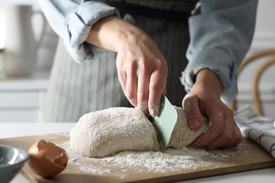 Photo of Woman cutting dough at white wooden table in kitchen, closeup