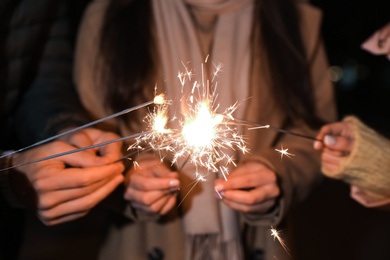 Photo of Group of people in warm clothes holding burning sparklers, closeup