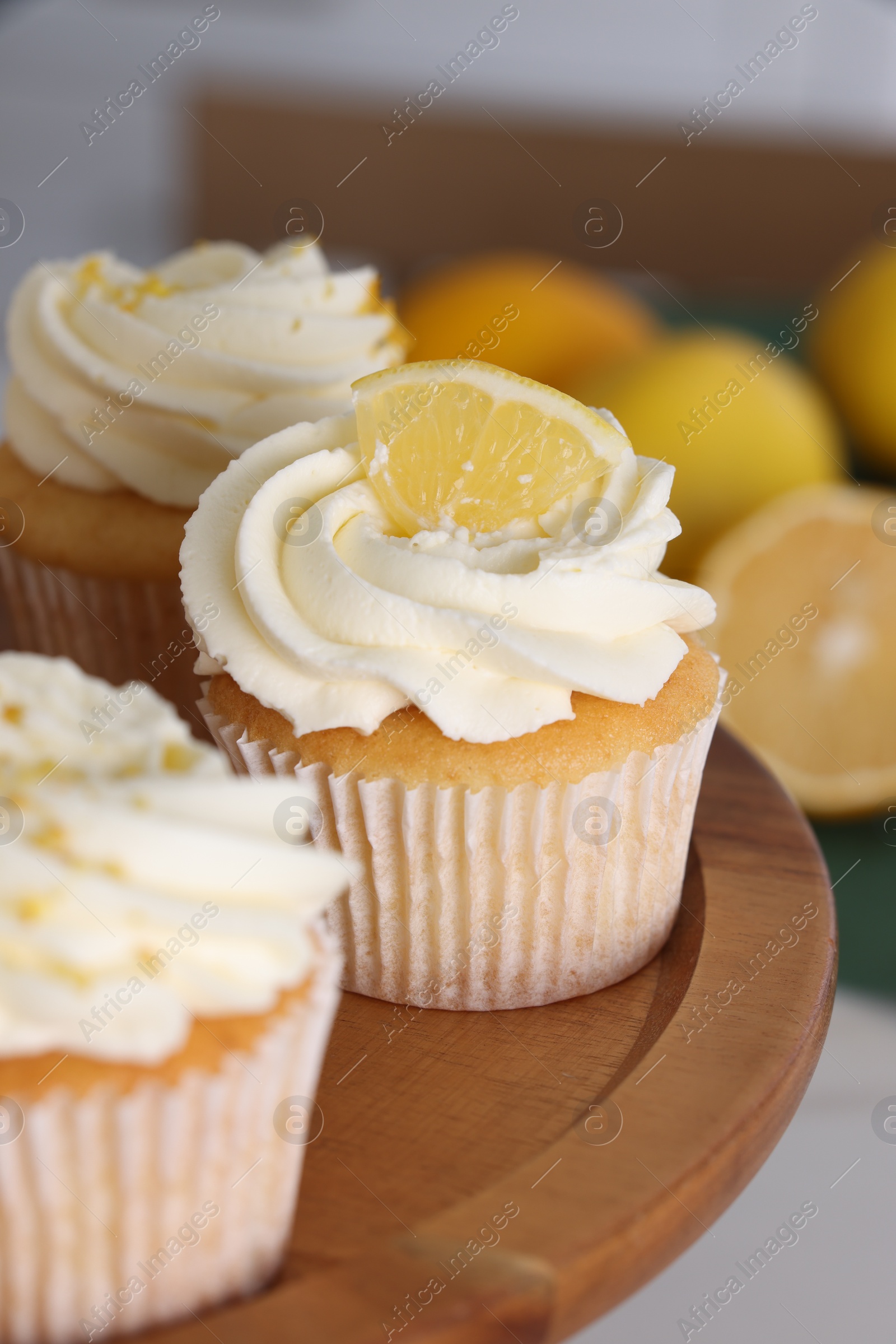 Photo of Delicious lemon cupcakes with white cream on wooden stand, closeup