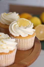 Photo of Delicious lemon cupcakes with white cream on wooden stand, closeup