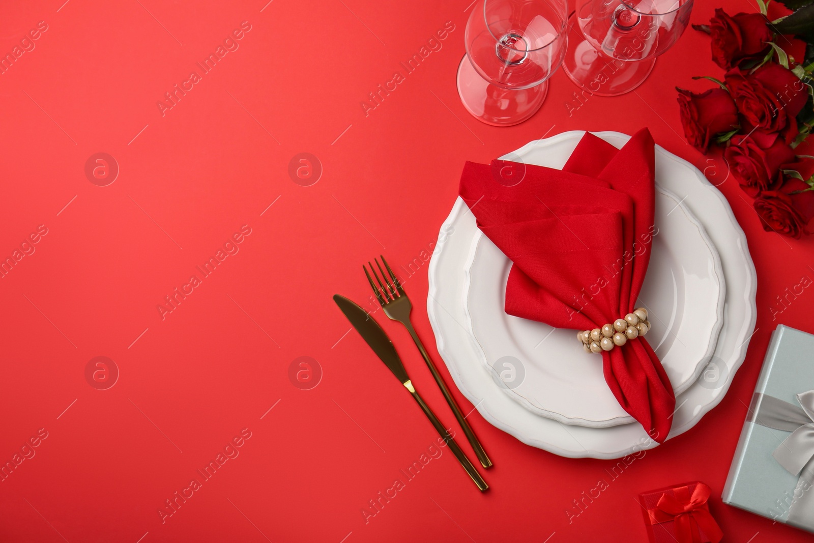 Photo of Place setting with gift boxes and bouquet of roses for romantic dinner on red table, flat lay. Space for text