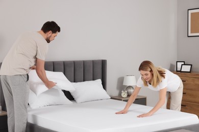Photo of Couple changing bed linens in room. Domestic chores