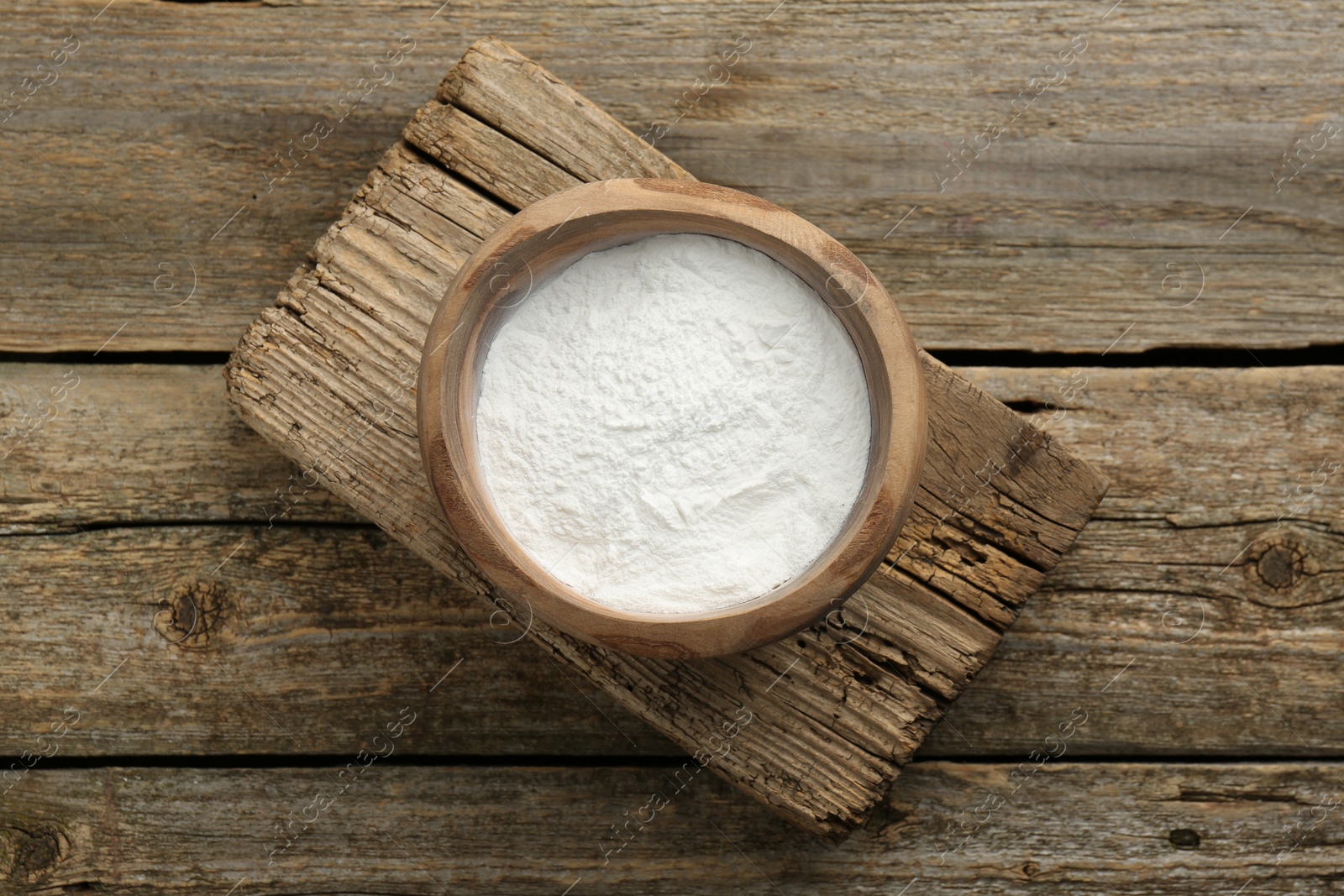 Photo of Baking powder in bowl on wooden table, top view