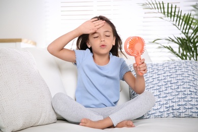 Little girl with portable fan suffering from heat at home. Summer season