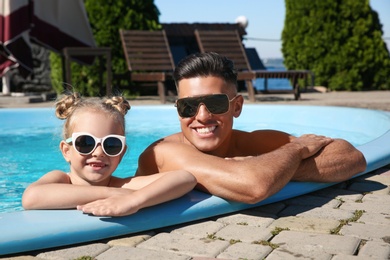 Happy man and his daughter in outdoor swimming pool on sunny summer day