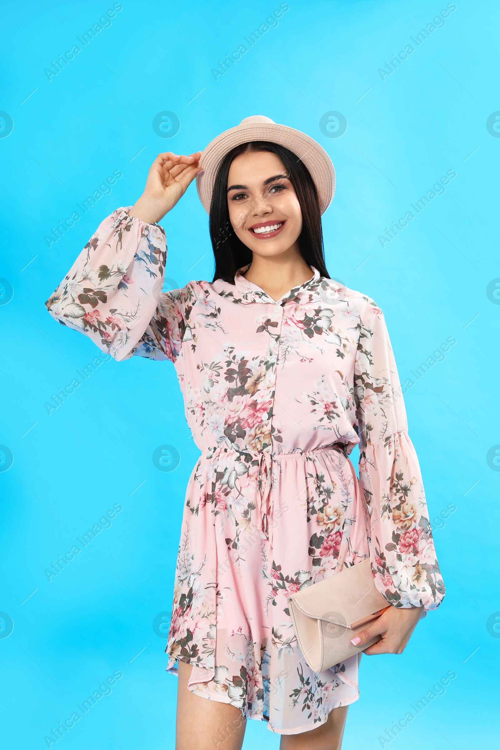 Photo of Young woman wearing floral print dress with clutch on light blue background