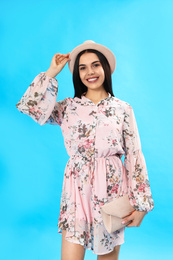 Photo of Young woman wearing floral print dress with clutch on light blue background