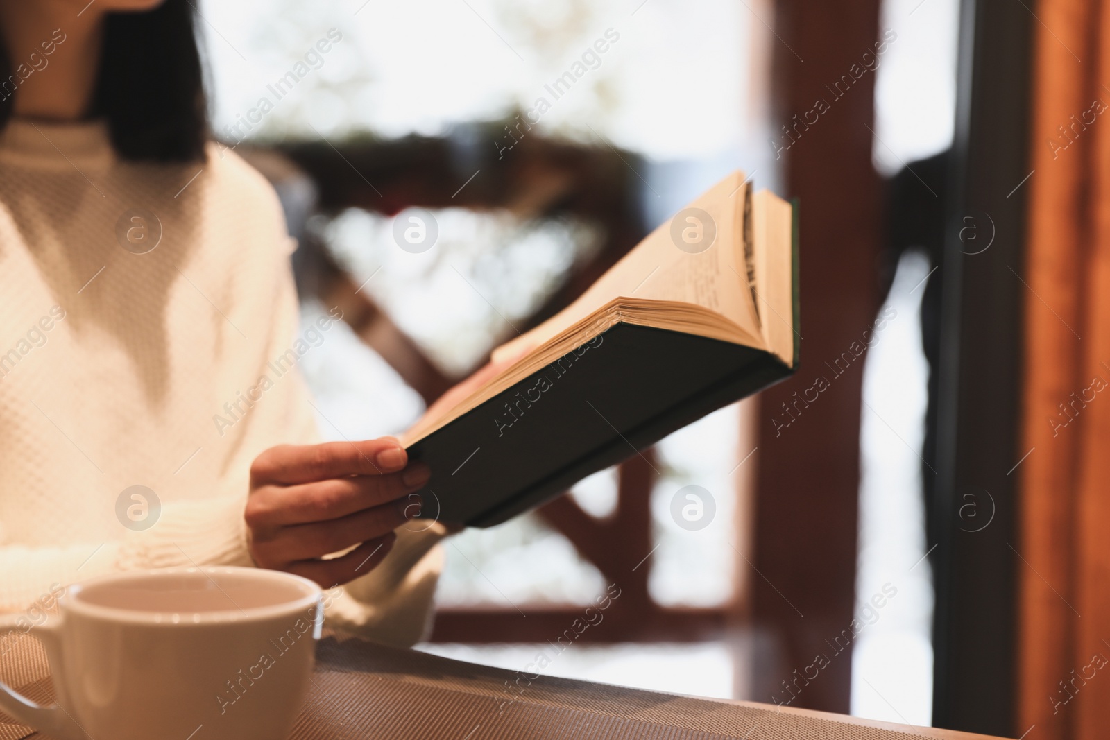 Photo of Woman with coffee reading book at wooden table, closeup