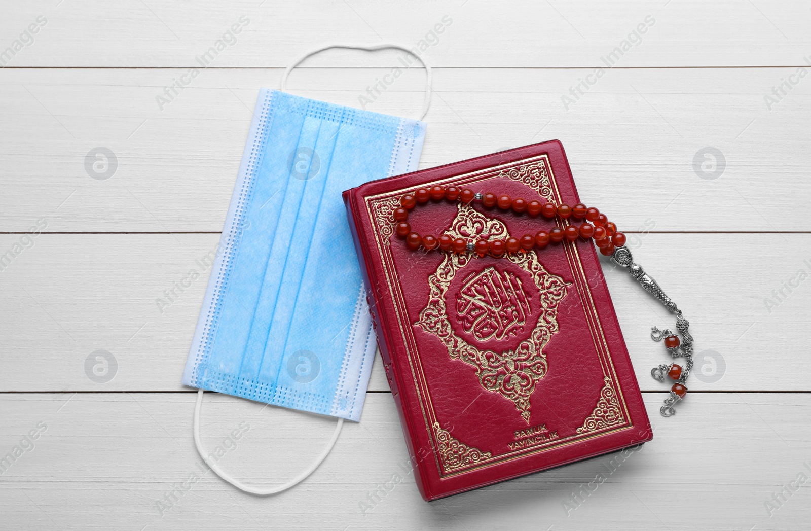Photo of Muslim prayer beads, Quran and protective mask on white wooden table, flat lay