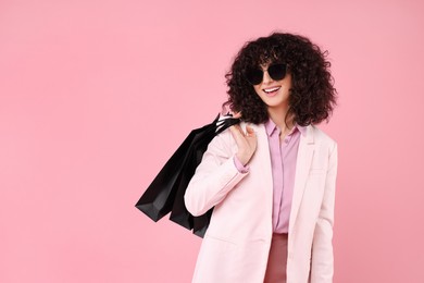 Happy young woman with shopping bags and stylish sunglasses on pink background. Space for text