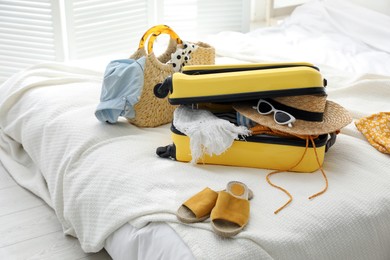 Photo of Open suitcase full of clothes, shoes and summer accessories on bed in room