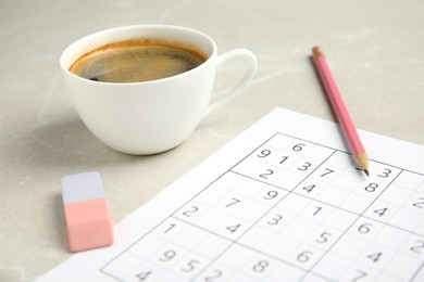 Sudoku, cup of coffee, eraser and pencil on light marble table, closeup