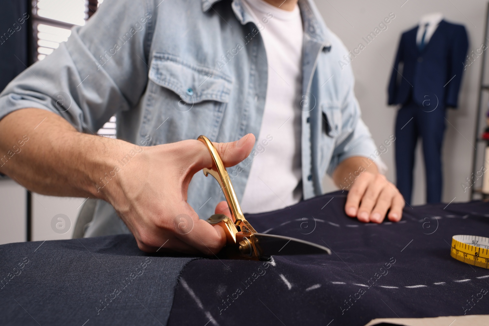 Photo of Tailor cutting fabric by following chalked sewing pattern at table in workshop, closeup