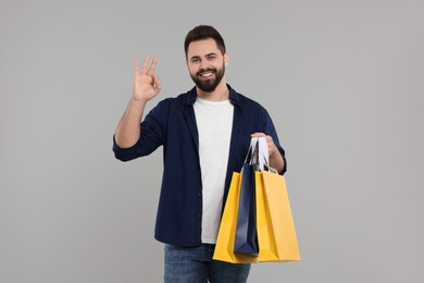 Happy man with many paper shopping bags showing ok gesture on grey background