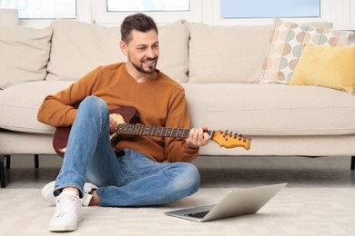 Photo of Man learning to play guitar with online music course at home. Time for hobby