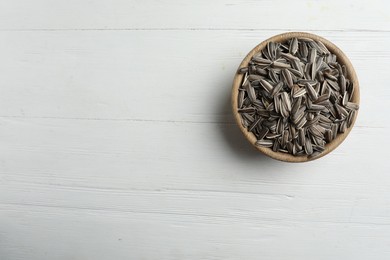 Photo of Raw sunflower seeds in bowl on white wooden table, top view. Space for text