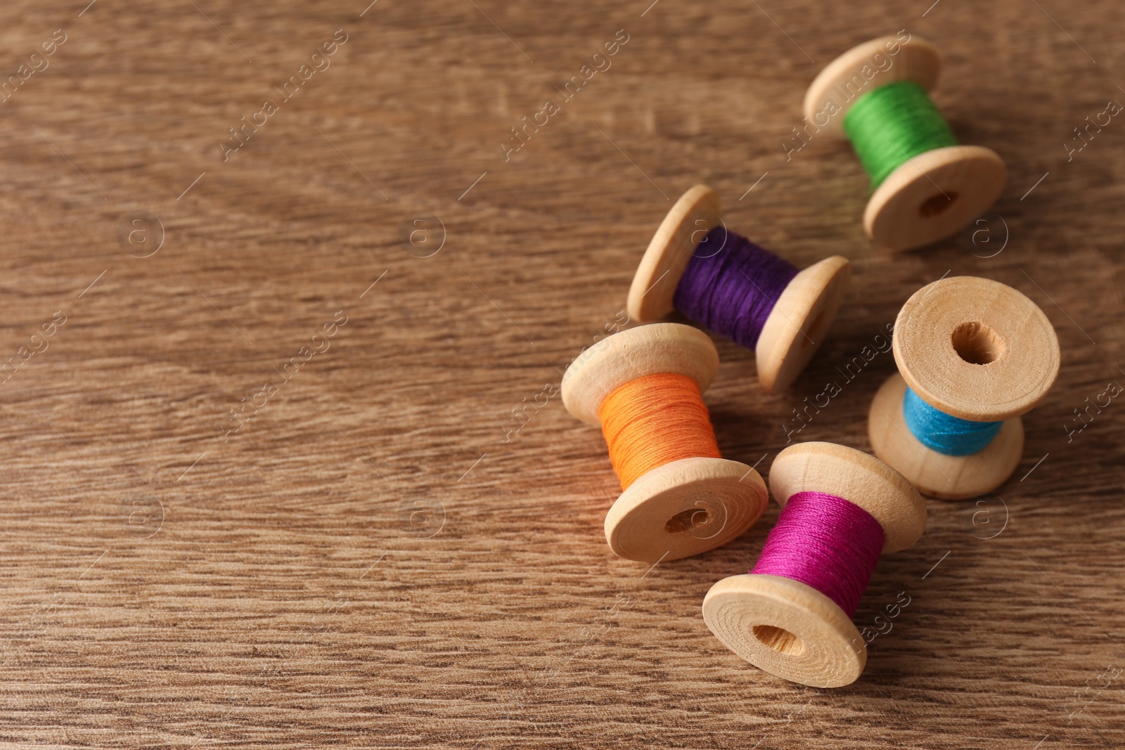 Photo of Set of color sewing threads on wooden table, space for text