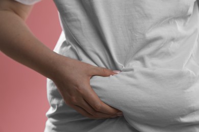 Woman touching belly fat on pink background, closeup. Overweight problem