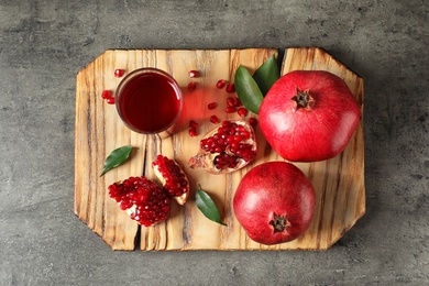 Photo of Board with glass of pomegranate juice and fresh fruits on grey background, top view