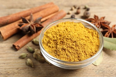 Photo of Curry powder in bowl and other spices on wooden table, closeup