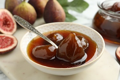 Photo of Bowl of tasty sweet jam and fresh figs on white marble table