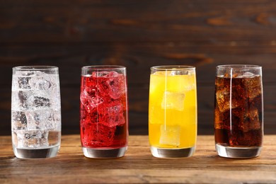 Photo of Glasses of different refreshing soda water with ice cubes on wooden table