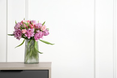 Photo of Beautiful bouquet of colorful tulip flowers in vase on wooden bedside table