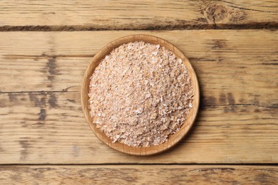 Photo of Bowl of wheat bran on wooden table, top view