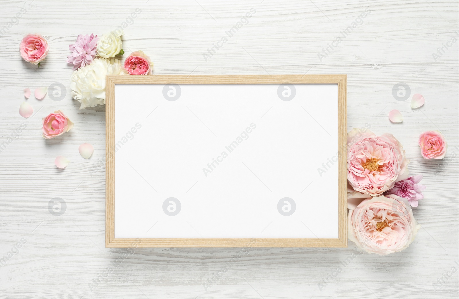 Photo of Empty photo frame and beautiful flowers on white wooden table, flat lay. Space for design