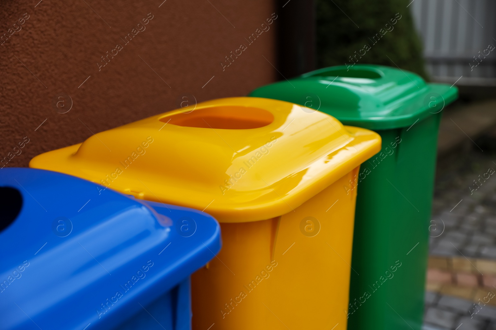 Photo of Many color recycling bins near brown wall outdoors, closeup