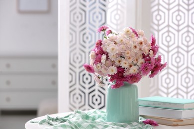 Photo of Vase with beautiful bouquet, books and checkered cloth on white table in room. Space for text