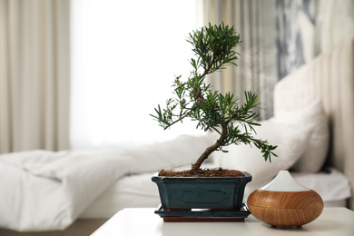 Photo of Japanese bonsai plant and oil diffuser on table in bedroom, space for text. Creating zen atmosphere at home