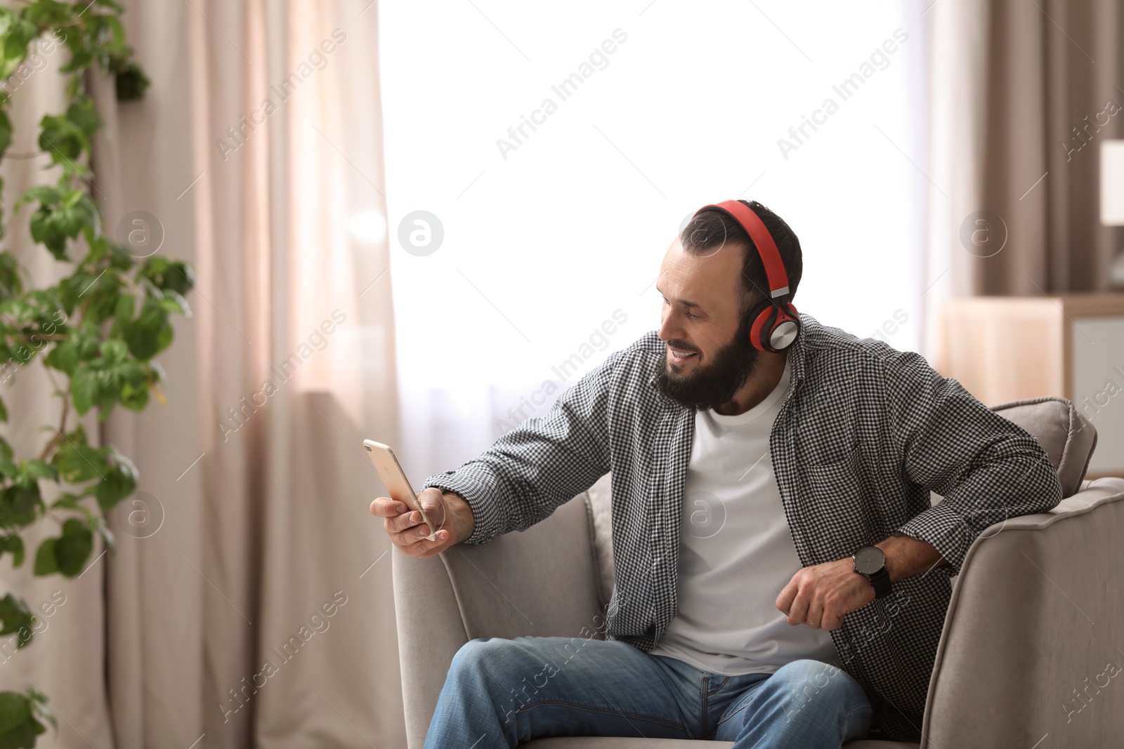 Photo of Mature man with headphones and mobile device resting in armchair at home