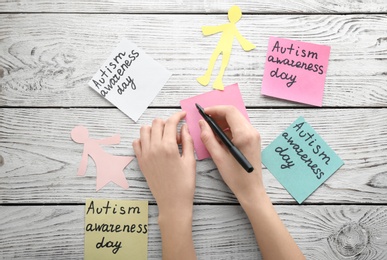 Woman and sticky notes with phrase "Autism awareness day" on wooden background