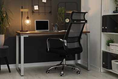 Photo of Cozy workplace with modern laptop on desk and comfortable chair at home