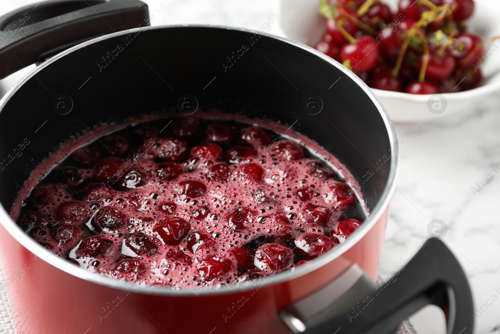 Photo of Pot with cherries in sugar syrup on table, closeup. Making delicious jam