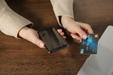 Photo of Online payment. Woman with smartphone using credit card at wooden table, closeup