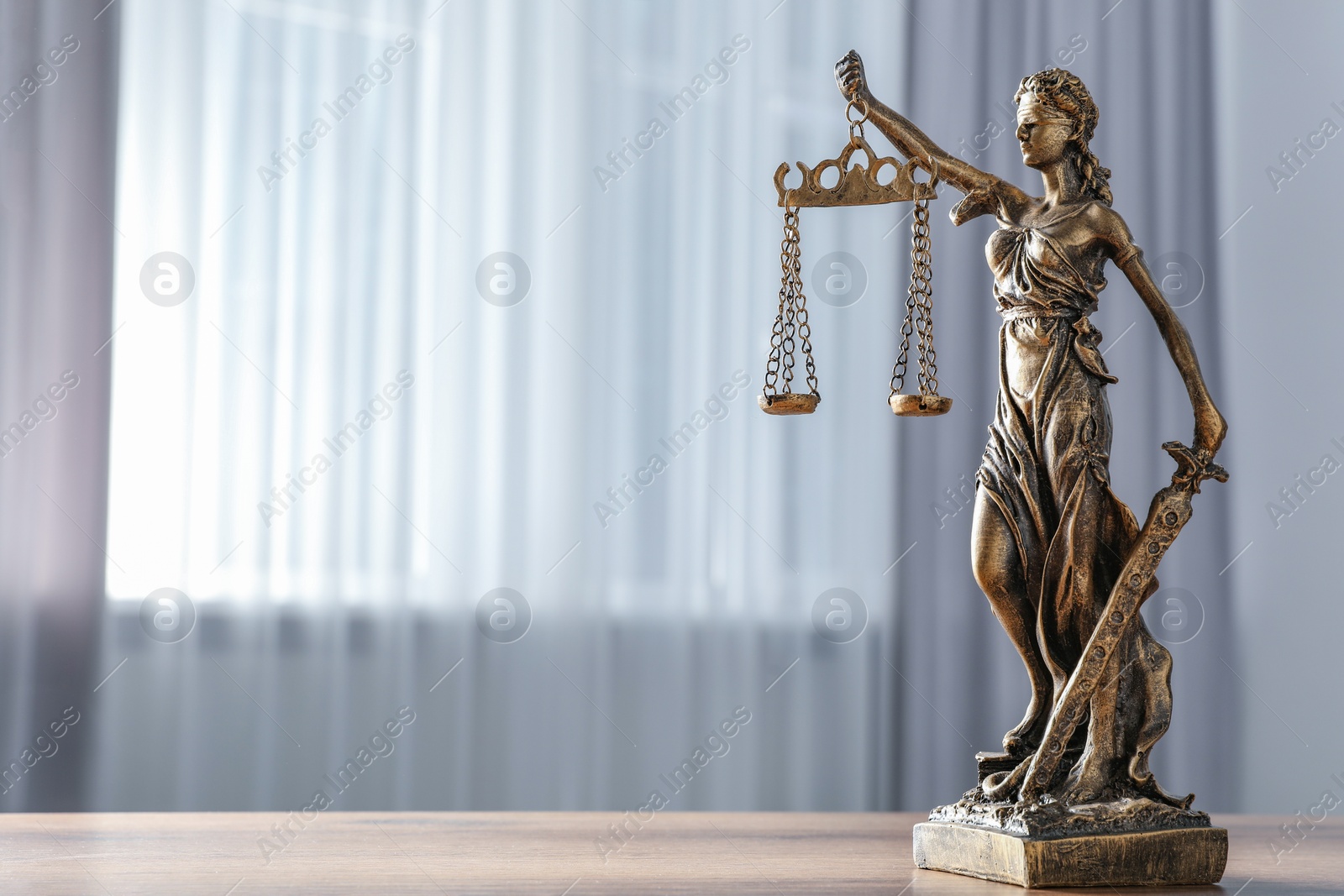 Photo of Figure of Lady Justice on wooden table indoors, space for text. Symbol of fair treatment under law