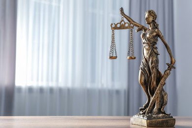 Figure of Lady Justice on wooden table indoors, space for text. Symbol of fair treatment under law