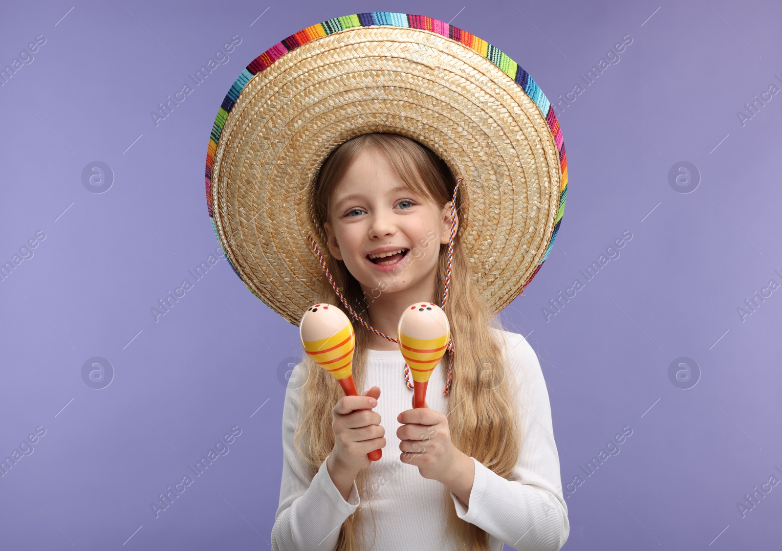 Photo of Cute girl in Mexican sombrero hat with maracas on purple background