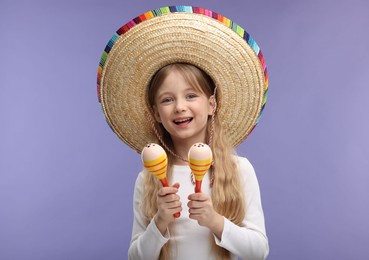 Cute girl in Mexican sombrero hat with maracas on purple background