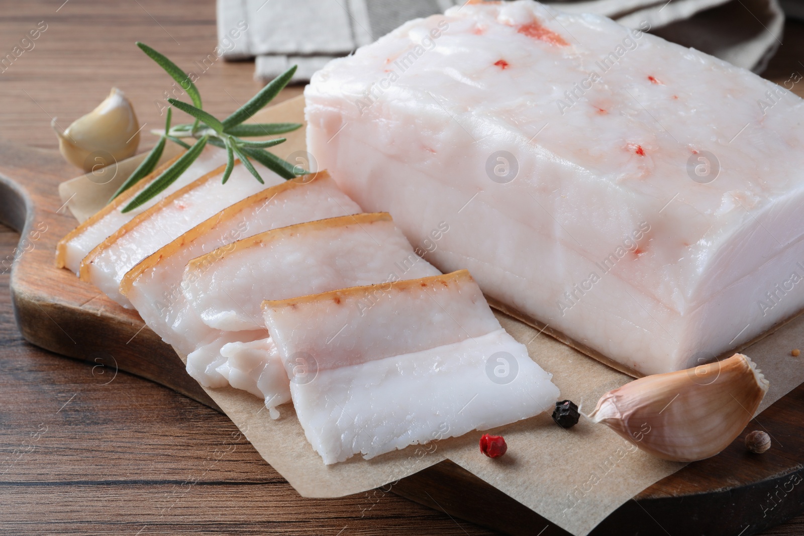 Photo of Pork fatback with rosemary, garlic and peppercorns on wooden table, closeup