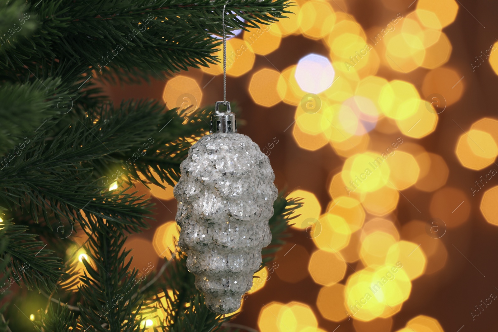 Photo of Beautiful cone shaped bauble hanging on Christmas tree against blurred festive lights, closeup