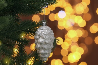 Photo of Beautiful cone shaped bauble hanging on Christmas tree against blurred festive lights, closeup